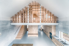 Interiér domu korunovaný obloukem v hřebeni střechy je jedním spojitým prostorem rozděleným vzdušnou knihovnou