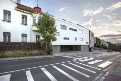 Pohled z ulice – objekt navazuje na sousední zástavbu, parter je materiálově odlišný, u řadových domů v okolí byl také zvýrazněn sokl stavby. Hlavní obytná podlaží jsou nad něj opticky vyzdvižena.