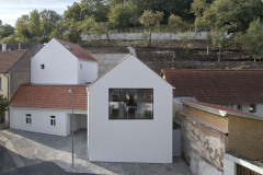 Místo má genius loci ulice v někdejší vesnici za Prahou. Původní domek zůstal zachován, architekti dále pracovali s podobnými hmotami. Rodinný dům tedy tvoří tři objekty, novostavby jsou umístěny směrem do svahu