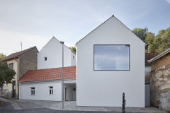 Místo má genius loci ulice v někdejší vesnici za Prahou. Původní domek zůstal zachován, architekti dále pracovali s podobnými hmotami. Rodinný dům tedy tvoří tři objekty, novostavby jsou umístěny směrem do svahu