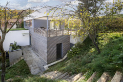 V původním hmotě stavby jsou pokoje a ložnice, nadstavěné patro se společenskou částí je zasunuté dozadu a přimyká se do svahu