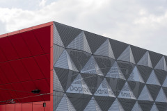 Vjezdový a výjezdní portál vytvářejí krytý prostor s červeným hliníkovým obkladem včetně skládacích motorických vrat, která jsou dokonale integrována do spárořezu obkladů