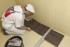 Dlaždice se pokládá na zazubenou plochu a přitlačí se. Postupně se osazuje dlažba po celé ploše s použitím obkladačských křížků, popř. klínků pro zajištění stejné tloušťky spár. U styku stěn je nutné dodržet dostatečné šířky dilatačních spár.