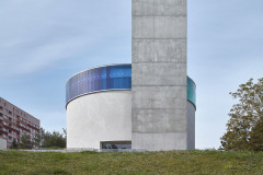 Okolním panelovým domům kostel nemůže konkurovat svou velikostí, proto vytváří dominantu jiné úrovně – na pozemku bylo vytýčeno plato, které vytvořilo sakrální okrsek